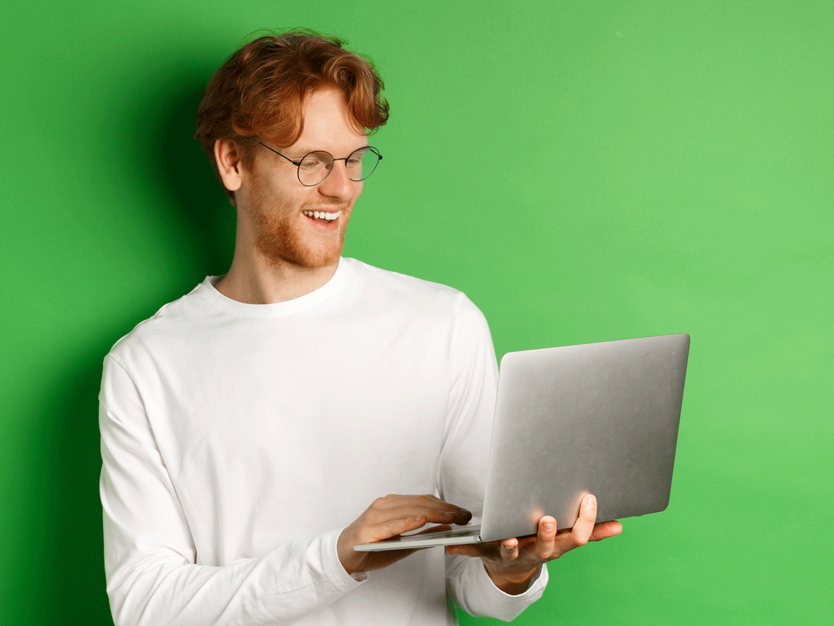 A male is shown holding a laptop in his hands, he is smiling as he looks at the screen. We cannot see the content of the screen.